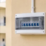 Surface-mounted white plastic distribution box with miniature circuit breakers on an exterior wall of an Indian residential building